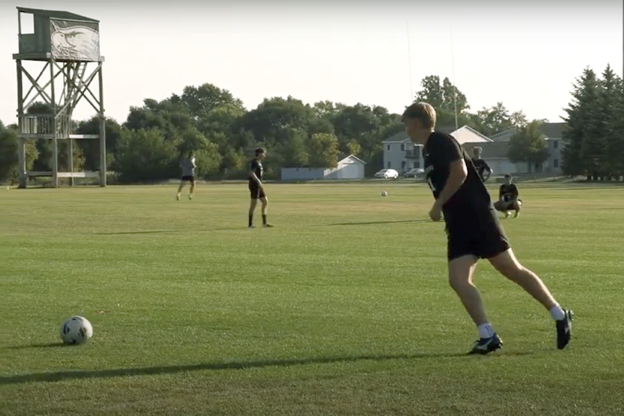 A soccer player hangs back to kick the ball onto the field.